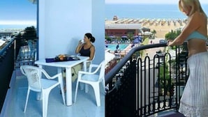 A balcony with a table and chairs, overlooking a pool and beach area. - Holiday apartment with air conditioning, balcony and pool (Bibione)