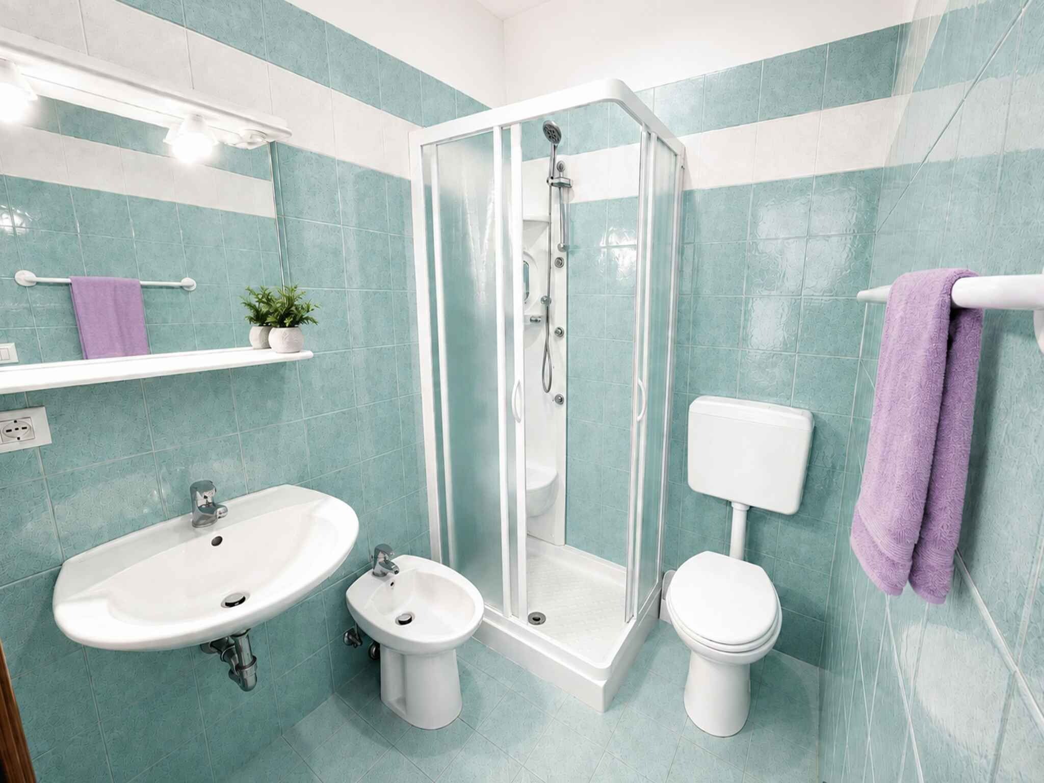 Et badeværelse med en glasafskærmet brusekabine, en hvid vask, en bidet og et toilet.
