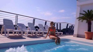 Ein Poolbereich mit Liegestühlen und einer Person, die am Pool sitzt.
