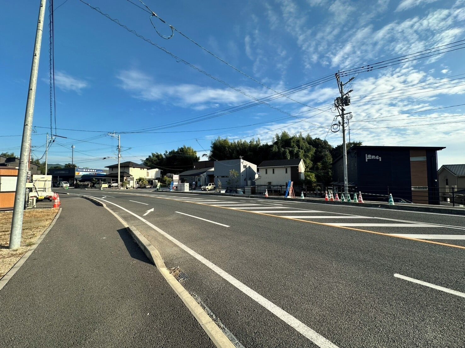 A wide road with multiple lanes, power lines overhead, and buildings on the sides.