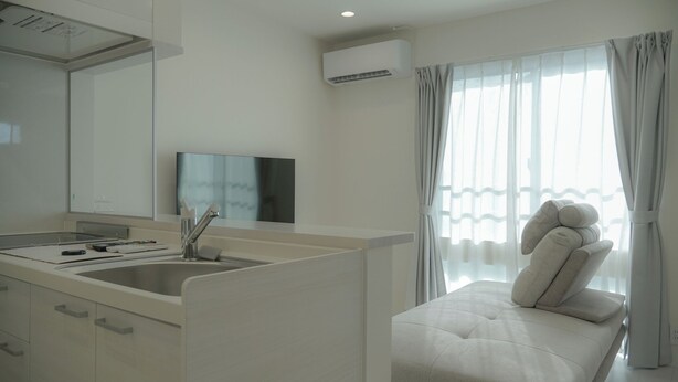 A modern hotel room with a kitchenette, a large mirror, a flat-screen TV, a sofa with pillows, and a window with sheer curtains. - Opt Kuamaoto Mashiki (Mashiki)