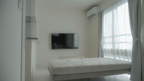 A minimalist bedroom with a bed, a mounted TV, and an air conditioning unit. - Opt Kuamaoto Mashiki (Mashiki)