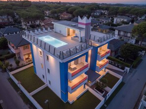 Un edificio moderno de varios pisos con piscina en la azotea, balcones y una característica arquitectónica distintiva que recuerda a una corona.