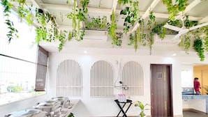 A modern hotel lobby with a long reception desk, arched windows, and hanging plants. - Hotel RG Residency (Varanasi)