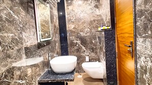 A bathroom with a marble wall, a sink, a toilet, and a shower. - Hotel RG Residency (Varanasi)