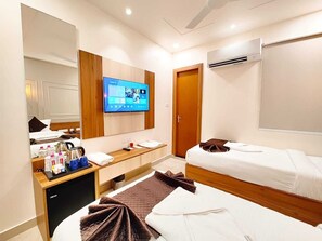 A hotel room with two beds, a TV, a desk with toiletries, and a wardrobe. - Hotel RG Residency (Varanasi)