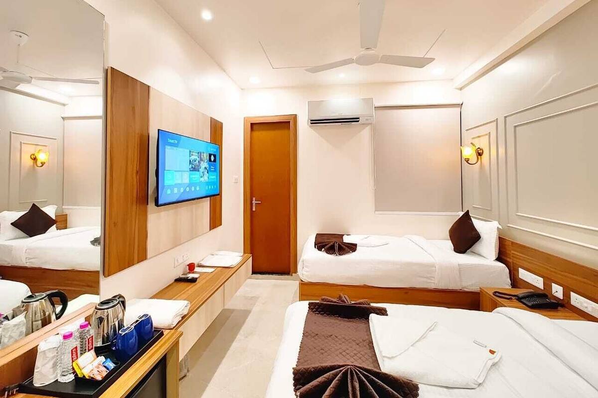 Quarto de hotel com duas camas, uma televisão, uma escrivaninha com chaleira e cafeteira, e um ventilador de teto.