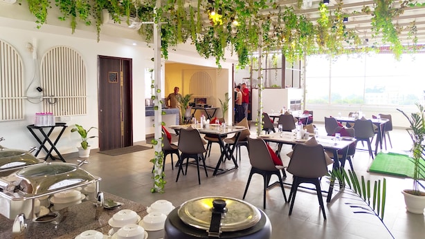 A restaurant with hanging plants, tables, chairs, and a buffet area. - Hotel RG Residency (Varanasi)