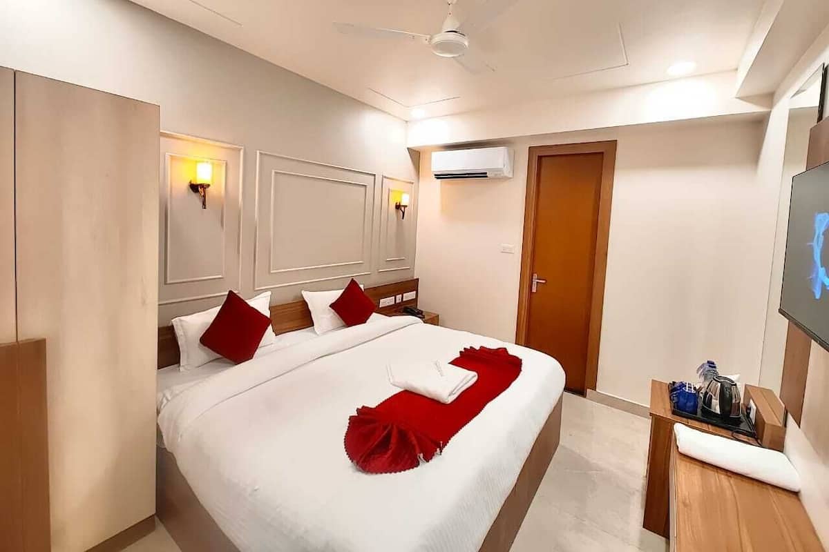 Quarto de hotel com uma cama grande, um ventilador de teto, um aparelho de ar condicionado, uma TV e uma mesinha com uma garrafa e uma xícara.