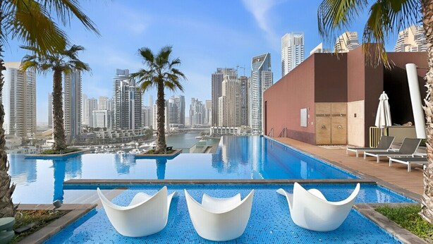 A swimming pool with modern chairs, palm trees, and a cityscape in the background. - Deluxe Marina Gate Suite w/ Sea & Ain Dubai View (Dubai)