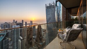 A balcony with a city view at sunset, a glass railing, a wicker chair, and a small table with a drink. - Deluxe Marina Gate Suite w/ Sea & Ain Dubai View (Dubai)
