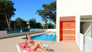 A poolside area with a lounge chair and a pool. - Holiday apartment with air conditioning, balcony and pool (Bibione)