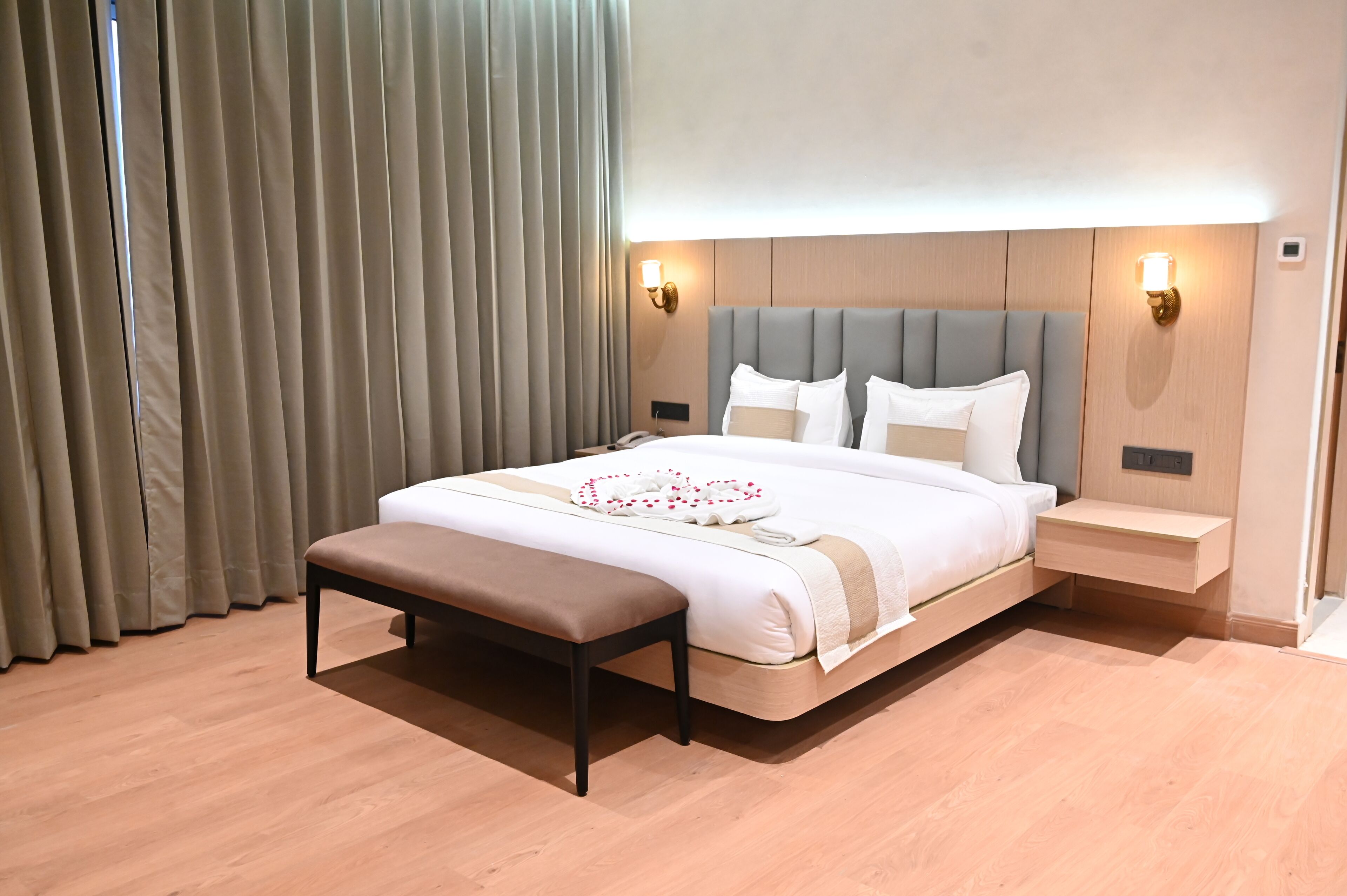 Ein Hotelzimmer mit Bett, Nachttischen, einer Bank und Vorhängen.