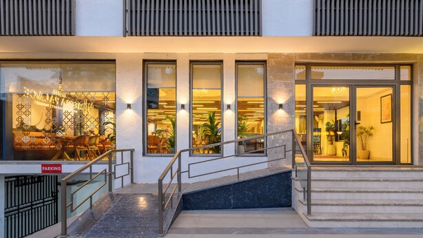 Entrada de hotel con escaleras, un letrero de estacionamiento y ventanas iluminadas.