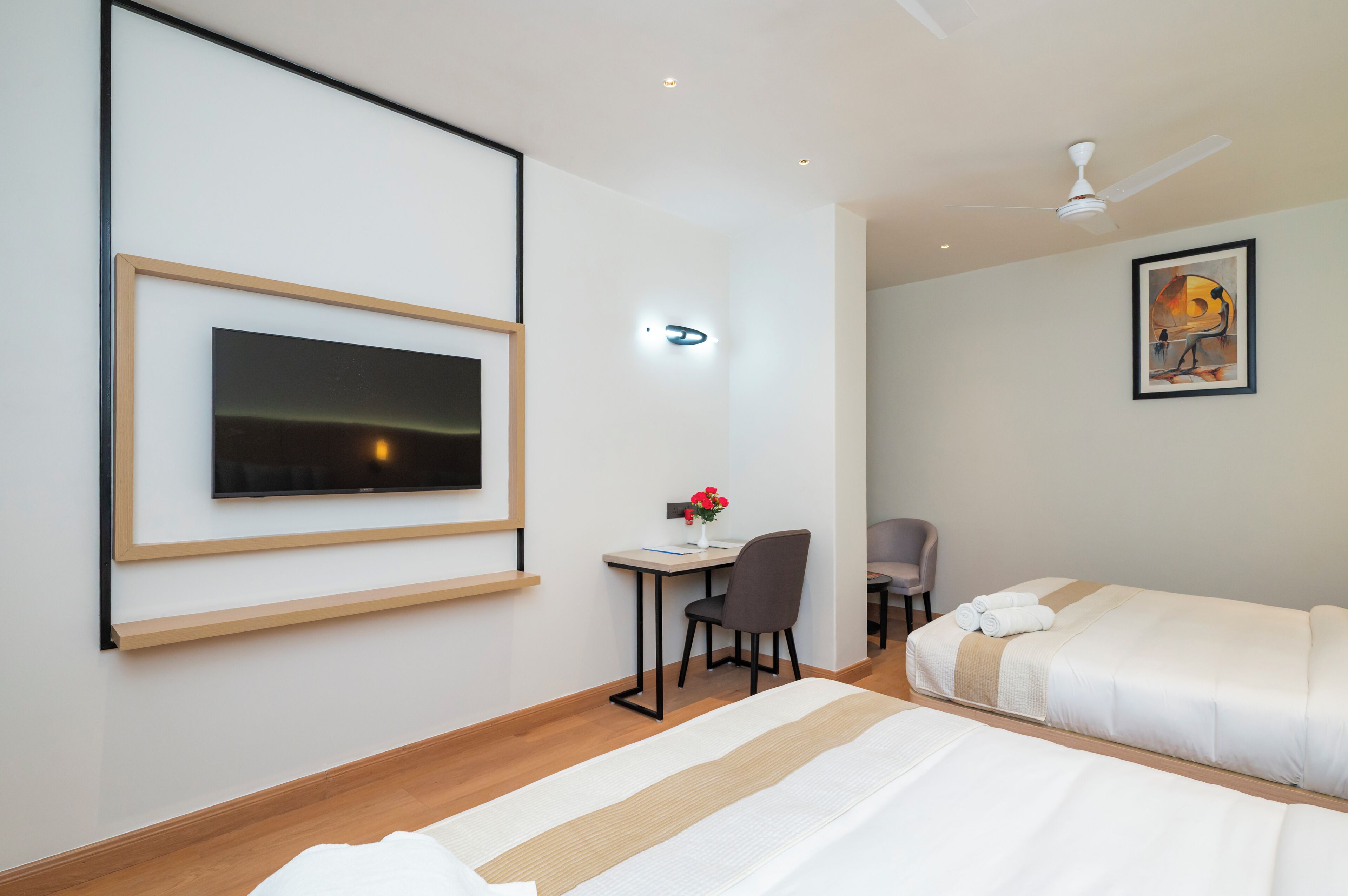 Ett hotellrum med en säng, ett skrivbord med en stol, en tv som är monterad på väggen och en takfläkt.