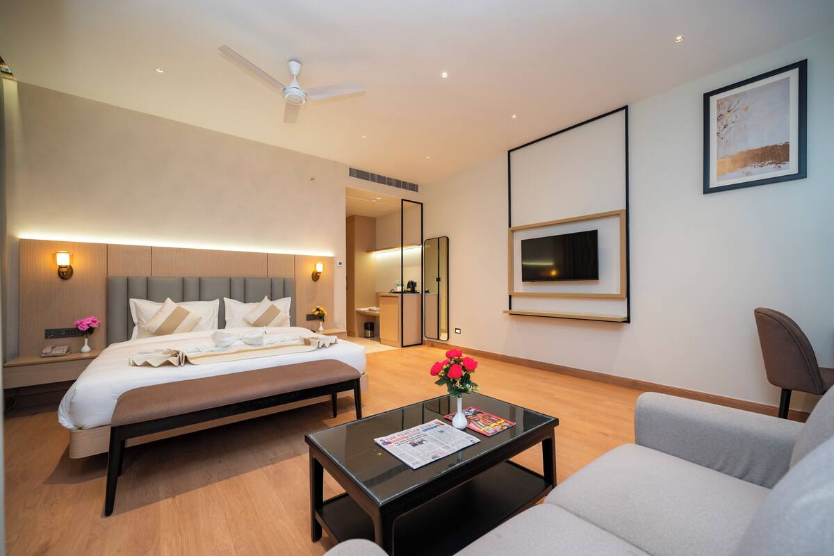 A modern hotel room with a bed, a sofa, a coffee table, a mirror, and a ceiling fan.