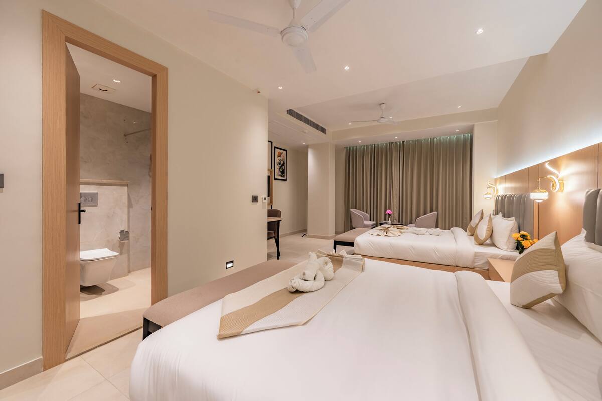 A hotel room with two beds, a bathroom, a ceiling fan, and a view of the city.