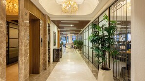 Un pasillo de hotel con piso de mármol, una lámpara de araña y plantas en macetas.