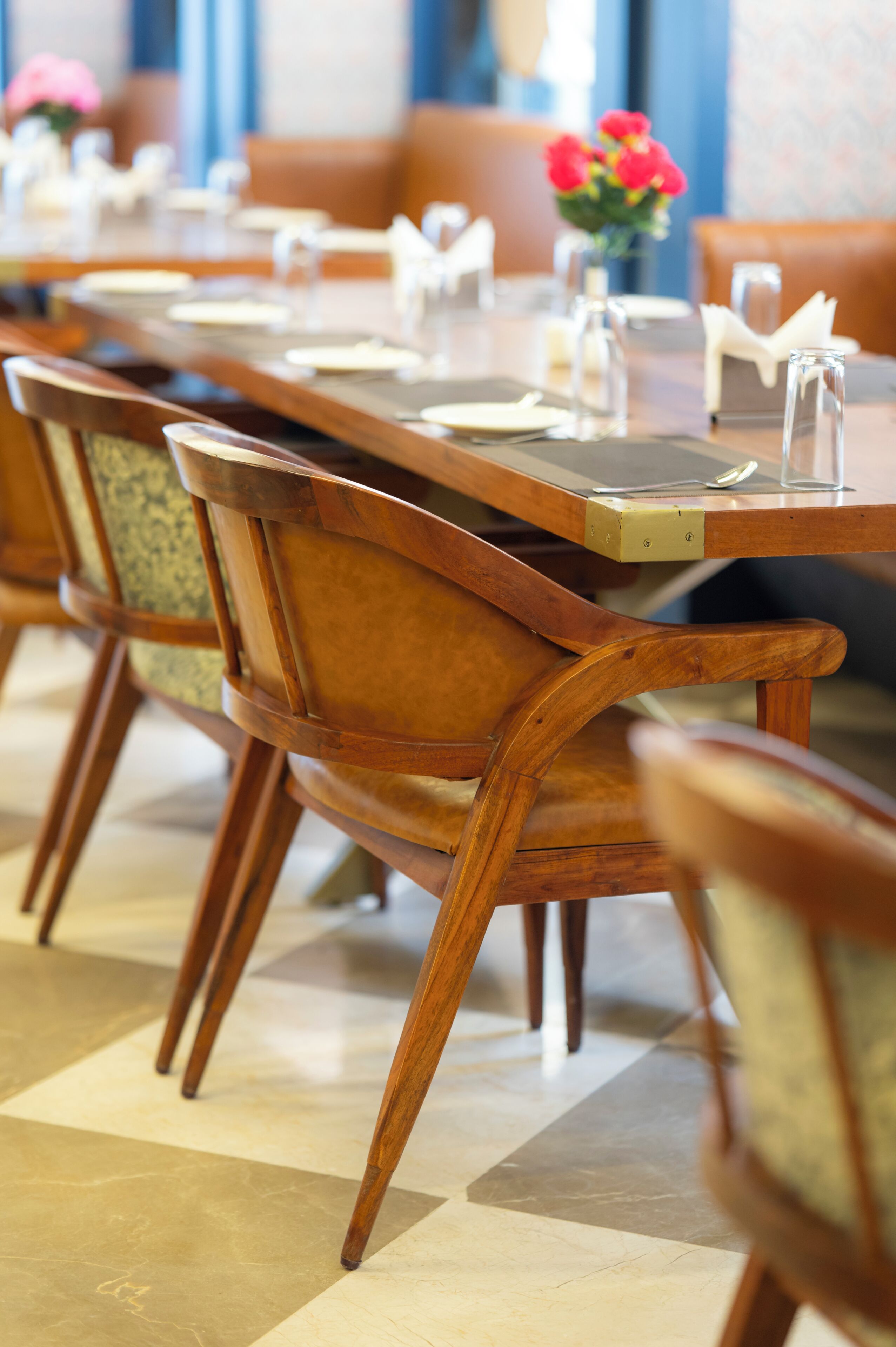 Un comedor con mesas y sillas de madera, suelo de baldosas y un jarrón con flores.