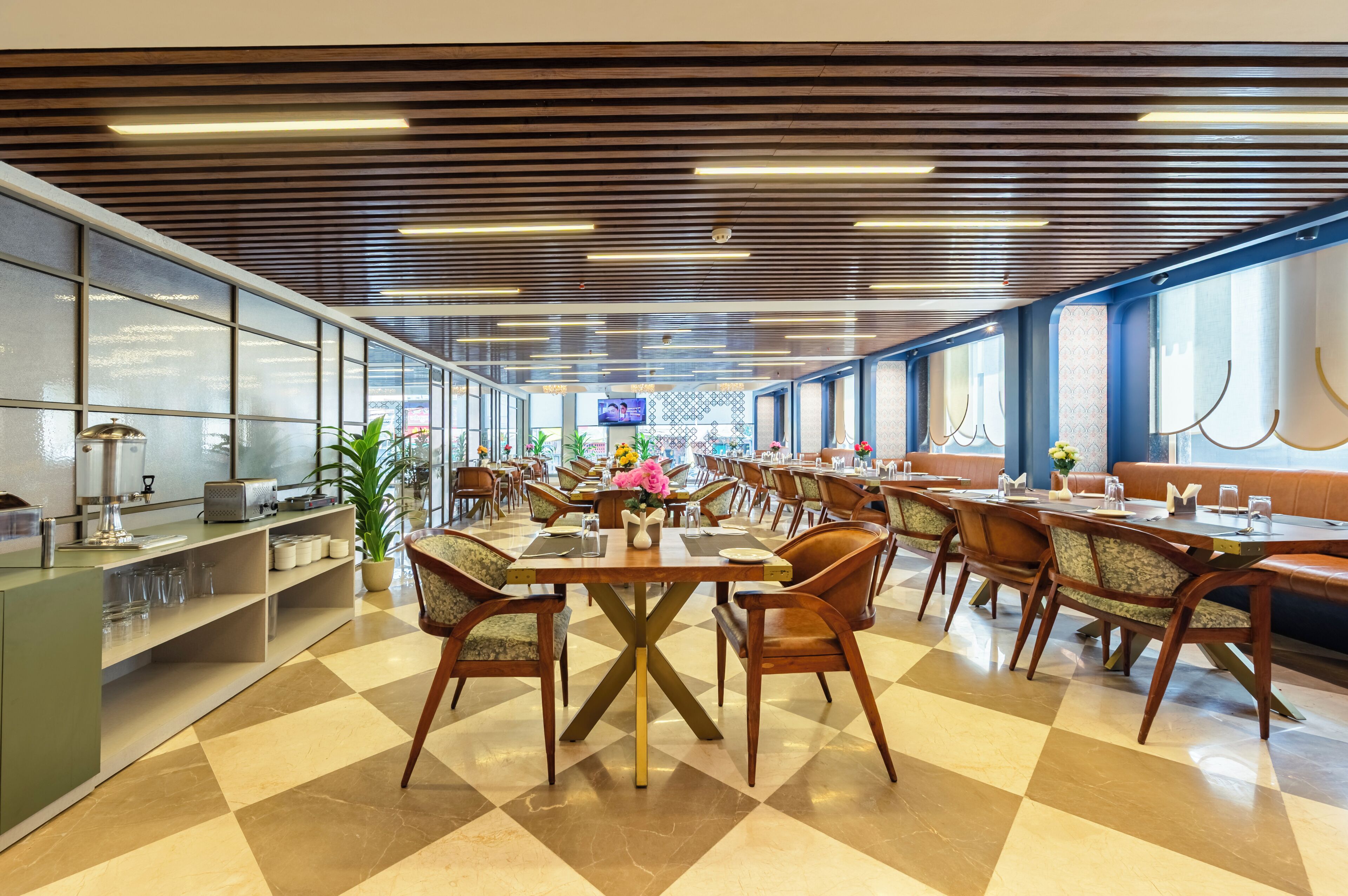 A spacious dining area with multiple tables and chairs, a counter with a coffee machine, and large windows along one wall.