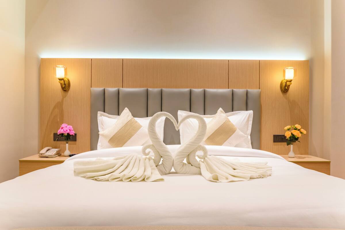 A hotel room with a large bed, two bedside tables, a wall-mounted phone, and two wall sconces.