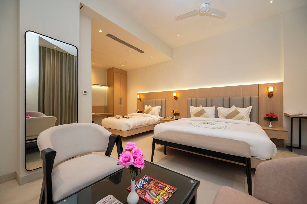 A hotel room with two beds, a sitting area with a table and chairs, a mirror, and a ceiling fan.