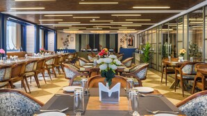 Un restaurante con mobiliario de madera, mesas dispuestas con platos, vasos y un jarrón de flores.