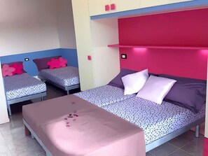 Une chambre avec deux lits simples, un lit plus grand et une petite table décorée de pétales de rose.
