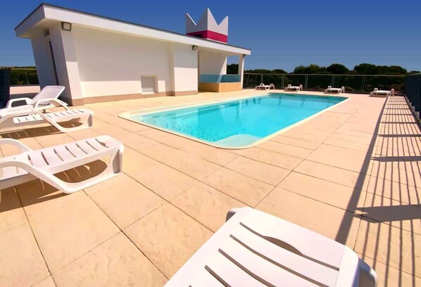 Une piscine sur le toit, dotée de chaises longues blanches et d’un petit bâtiment dont la façade est rehaussée d’une touche de rouge.