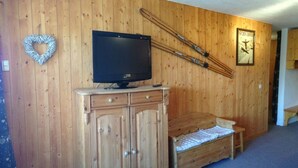 Une pi èce aux murs lambrés, avec un téléviseur posé sur un meuble, un banc et une affiche sur le thème du ski.