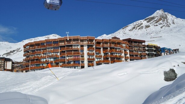 Un hôtel à plusieurs étages, doté de balcons, qui se dresse sur fond de montagnes enneigées.