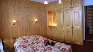 Une pièce aux murs recouverts de lambris en bois, un lit avec une couvre-lit à motifs, deux lampes fixées au mur et une armoire en bois dotée d’un miroir.