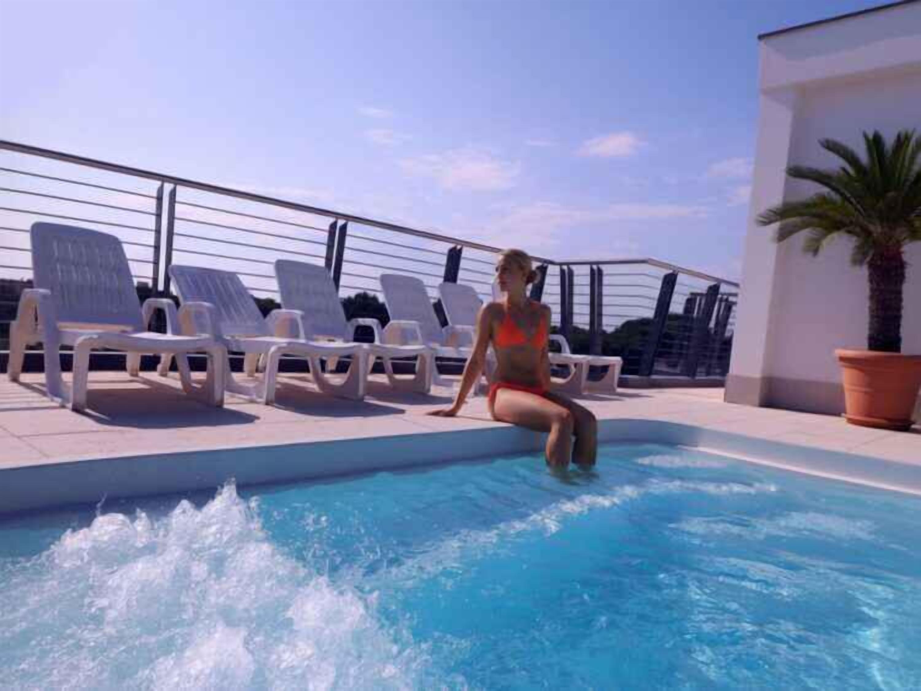 Área da piscina com espreguiçadeiras e uma pessoa sentada à beira da piscina.
