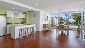 A modern kitchen with a central island, a dining area with a table and chairs, and a large sliding glass door leading to a balcony with a view. - Stylish 2-Bed with Terrace, 3-min Walk to Beach (Glenelg)