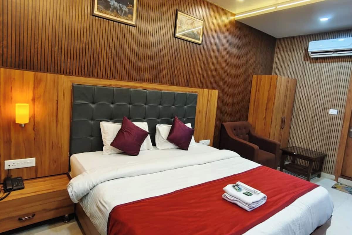 Una habitación de hotel con pared de paneles de madera, una cama grande con ropa de cama roja y blanca, un ventilador de techo y un aire acondicionado montado.