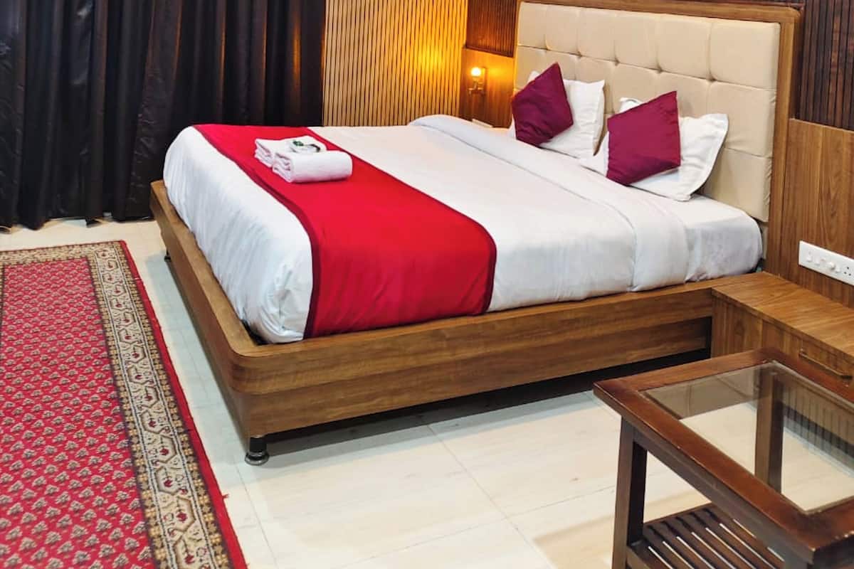 Una habitación de hotel con cama de madera, ropa de cama blanca y roja, ventilador de techo y alfombra roja con estampado.