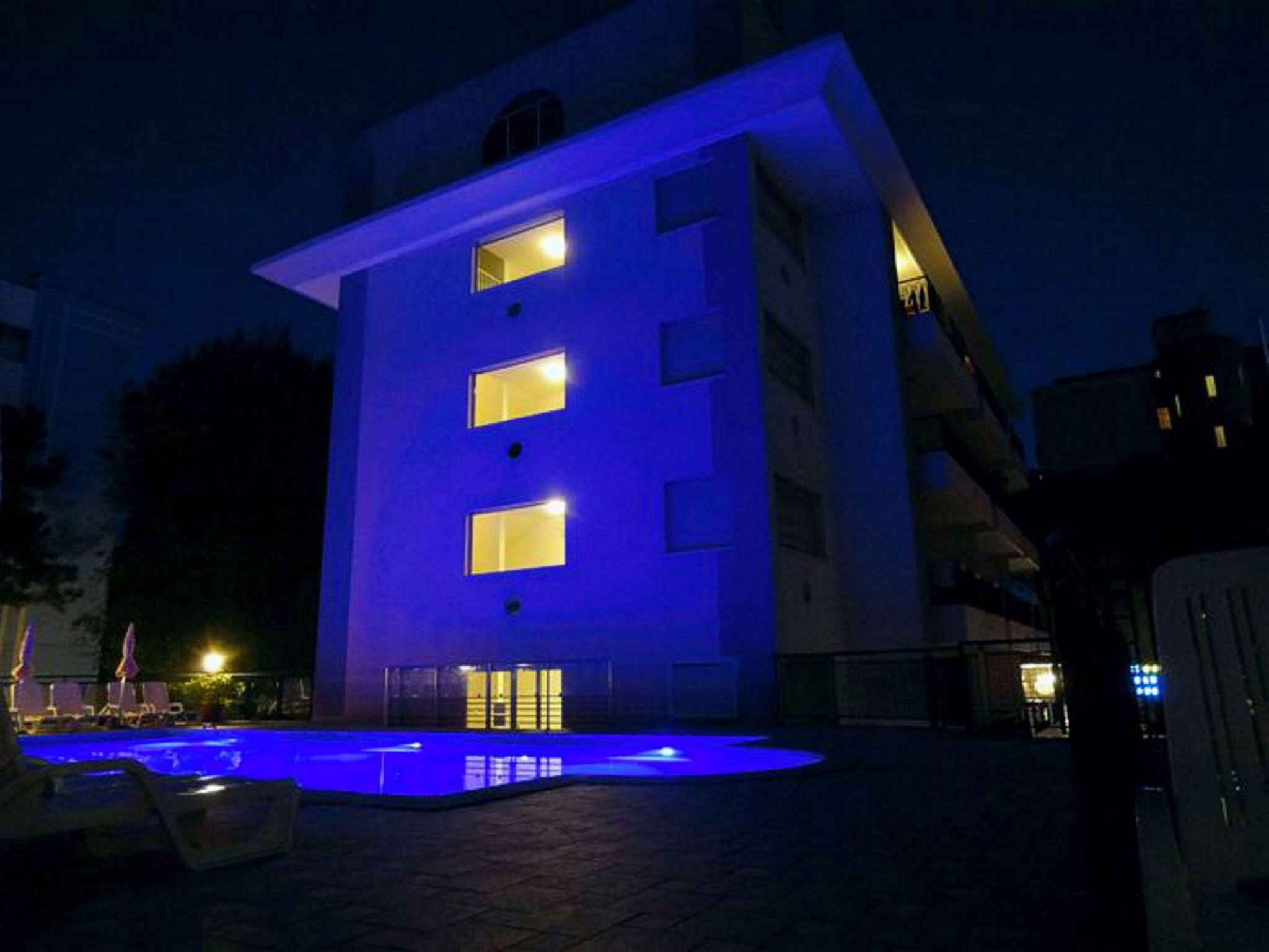 Un edificio con zona de piscina iluminada con luces azules por la noche.