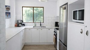 Uma cozinha moderna com armários brancos, uma geladeira de aço inoxidável e uma janela com vista para o verde.