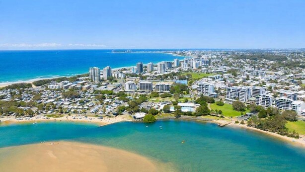 Paisagem costeira com edifícios altos, uma praia e um céu azul límpido.