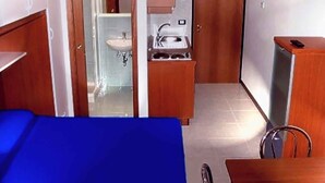 A compact hotel room with a bed, a small kitchenette, a bathroom with a sink and mirror, and a wooden wardrobe. - Studio with air conditioning, balcony and pool (Bibione)