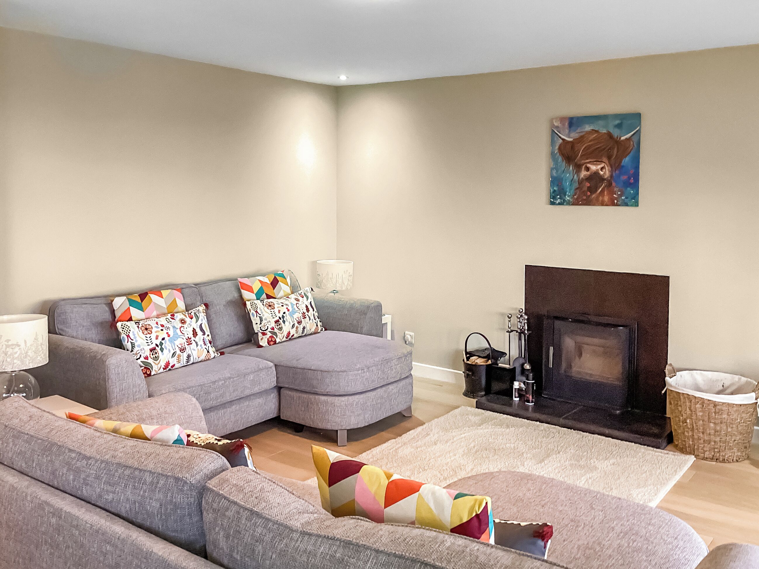 A living room with a grey sofa set, colorful cushions, a fireplace, and a painting on the wall.