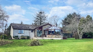Ein Haus mit einer Naturstein-Fassade, einem Wintergarten und einem gepflegten Rasen.