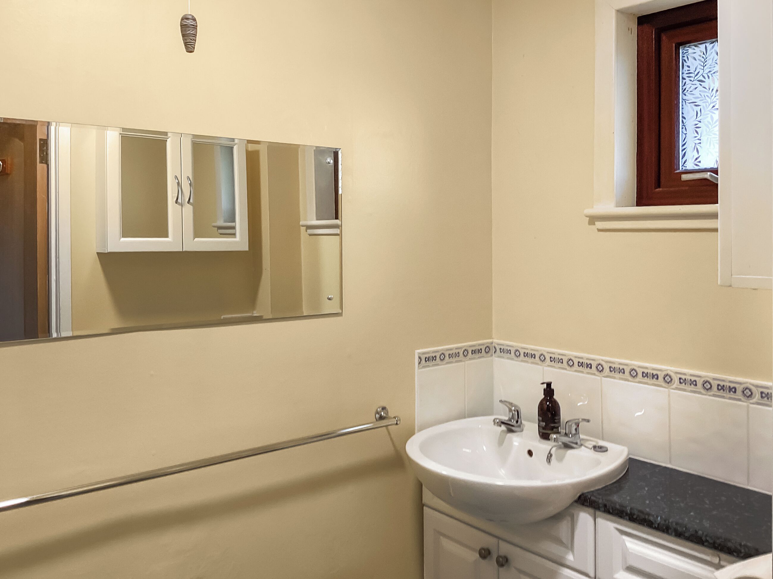Ein Badezimmer mit einem weißen Waschbecken, einem Spiegel und einem Fenster mit Milchglas.