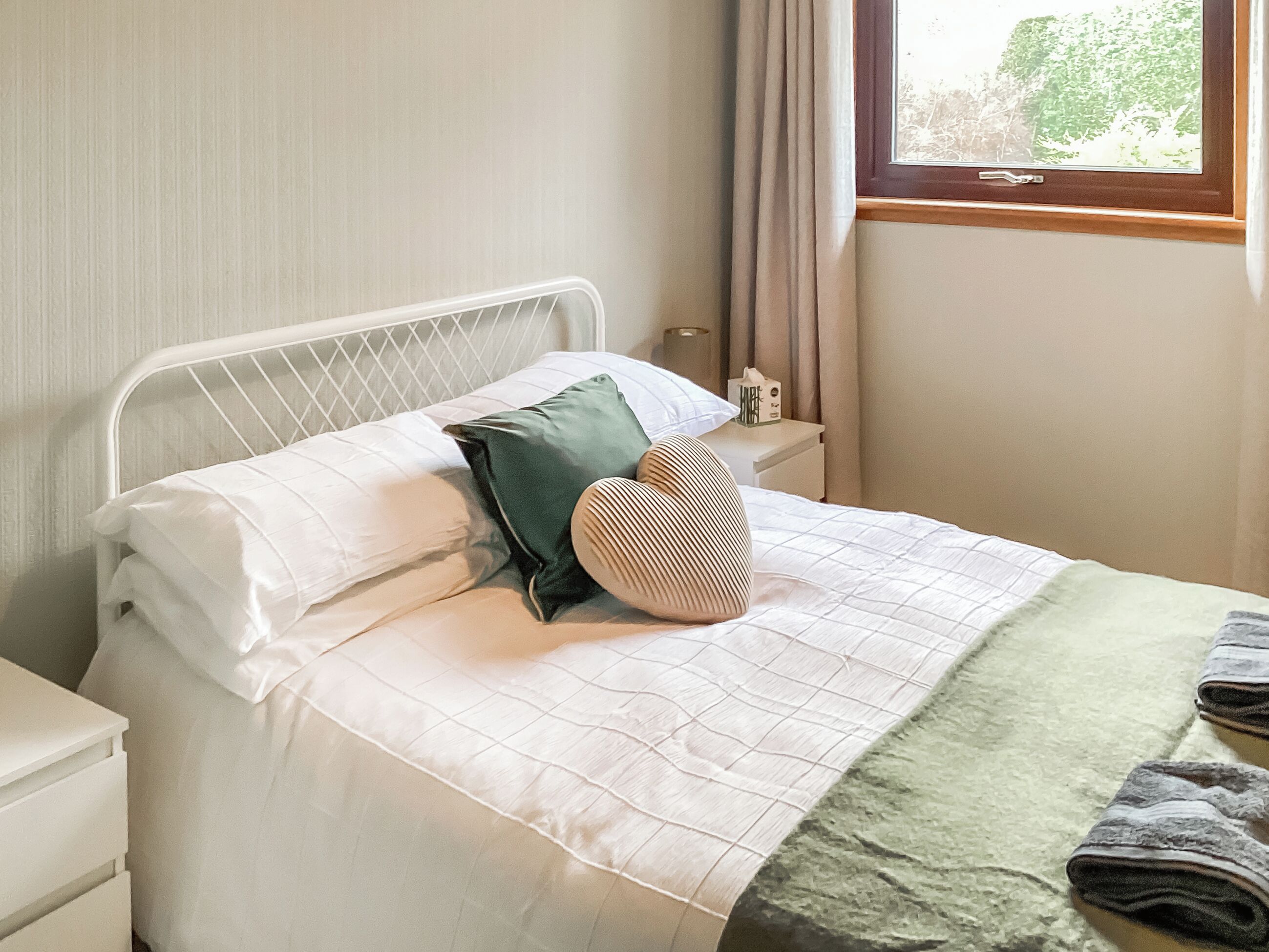 A neatly made bed with a white headboard, a green pillow, and a patterned pillow.