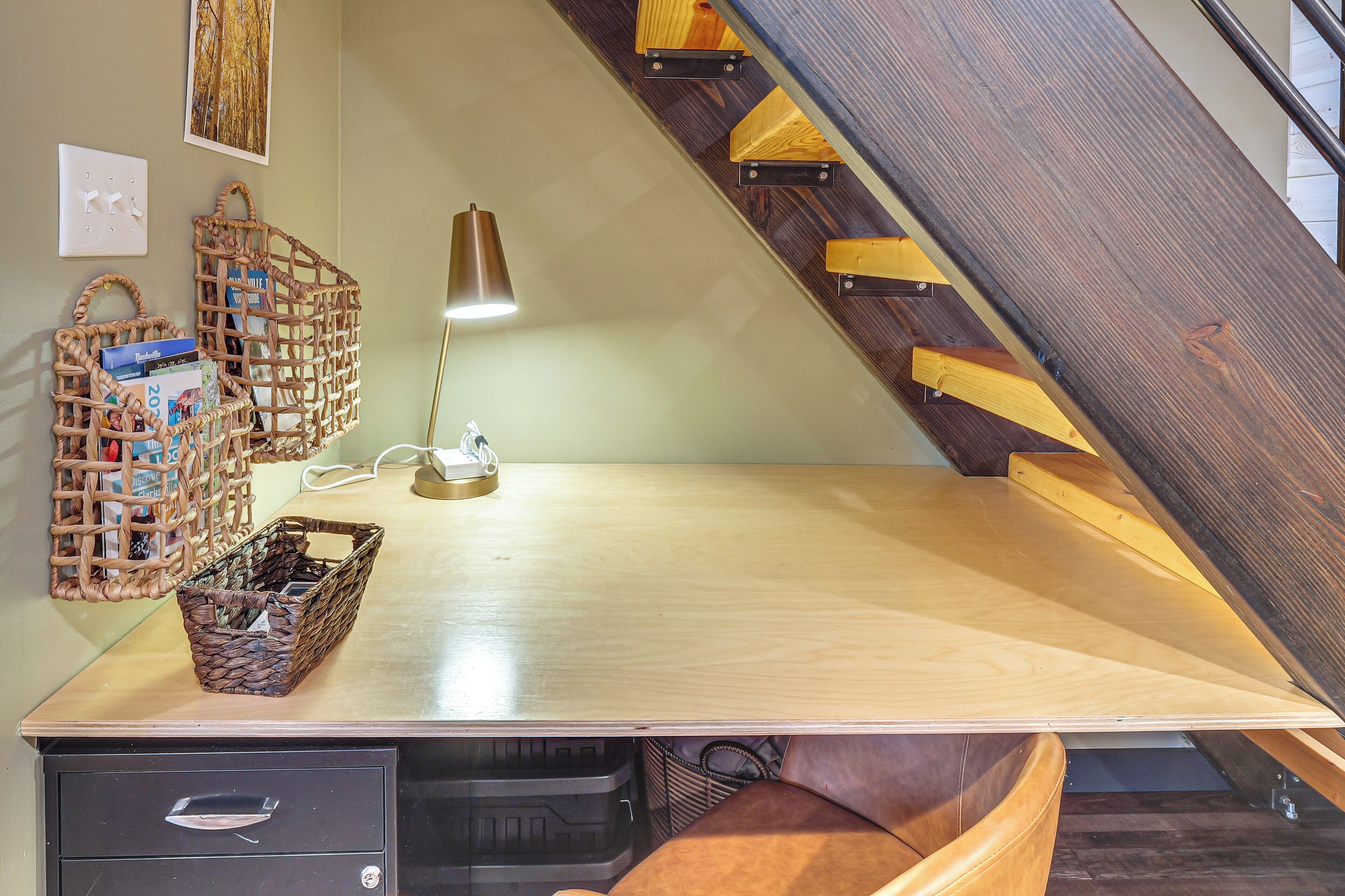 A workspace with a desk, wicker baskets, a lamp, and a staircase.