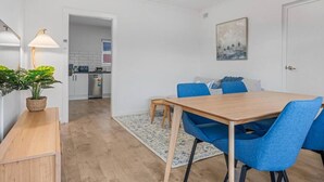 Un espace repas moderne avec une table en bois et des chaises bleues, une plante en pot et une cuisine en arrière-plan.