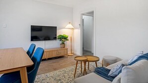 Un salon moderne avec un téléviseur à écran plat, une table à manger en bois, des chaises bleues, un canapé et un lampadaire.