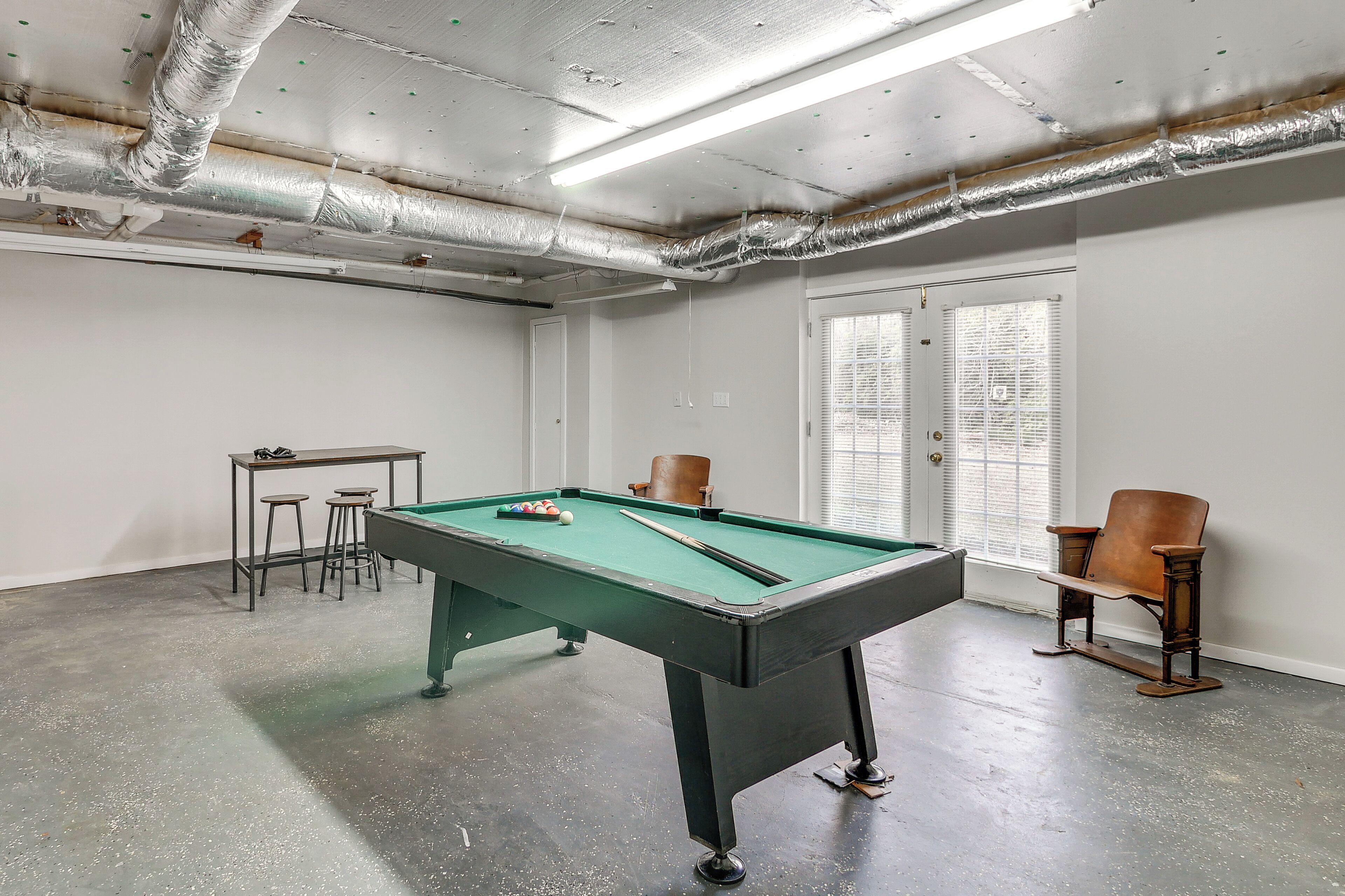Een pooltafel, stoelen, een kleine tafel en een raam met jaloezieën.