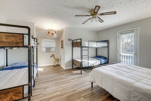 Una habitación con literas, ventilador de techo, ventana con persianas y una pequeña silla de madera.
