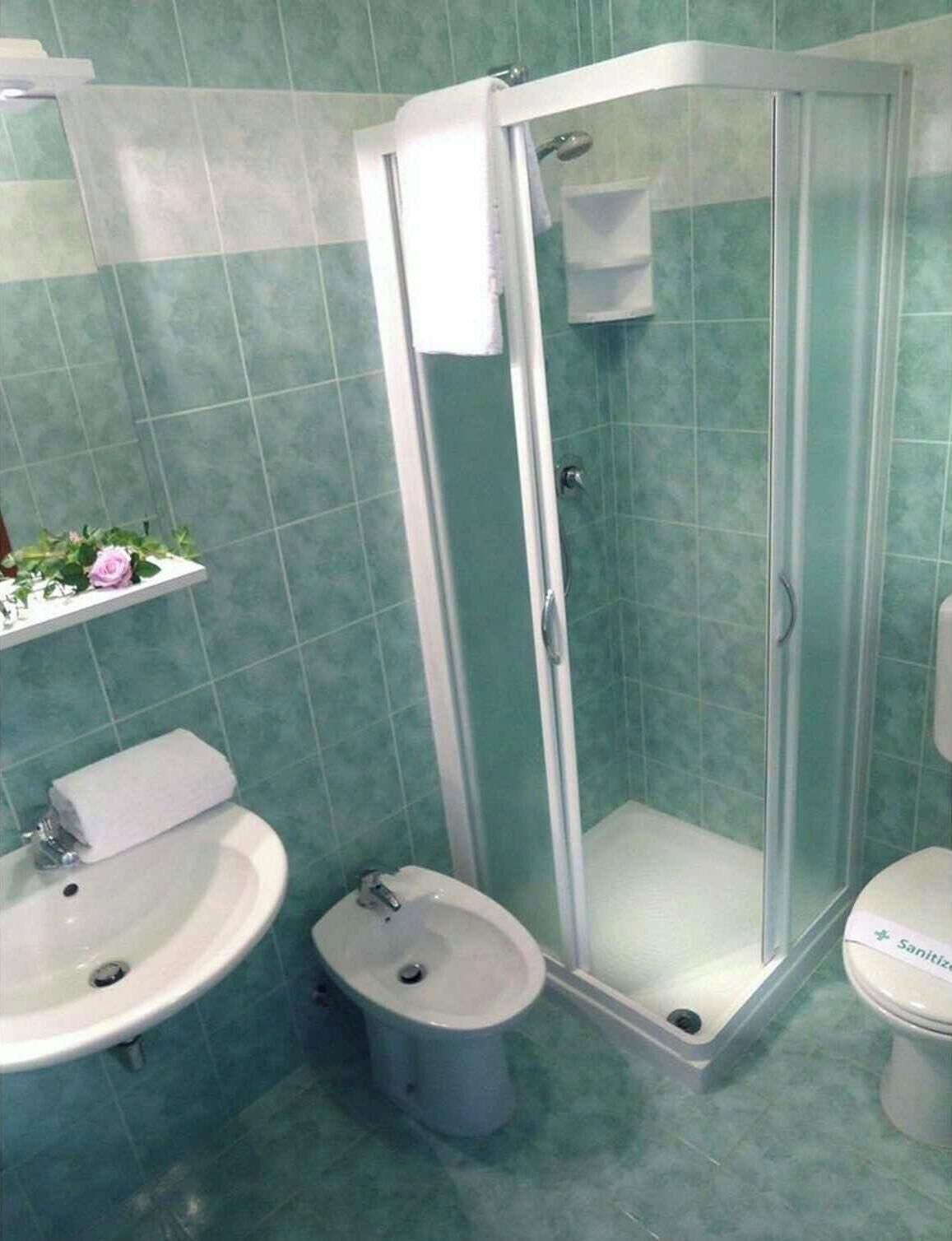 Ett badrum med en dusch som är avskärmad med glasväggar, ett handfat, en toalett och en hylla med ett handduk och en växt.